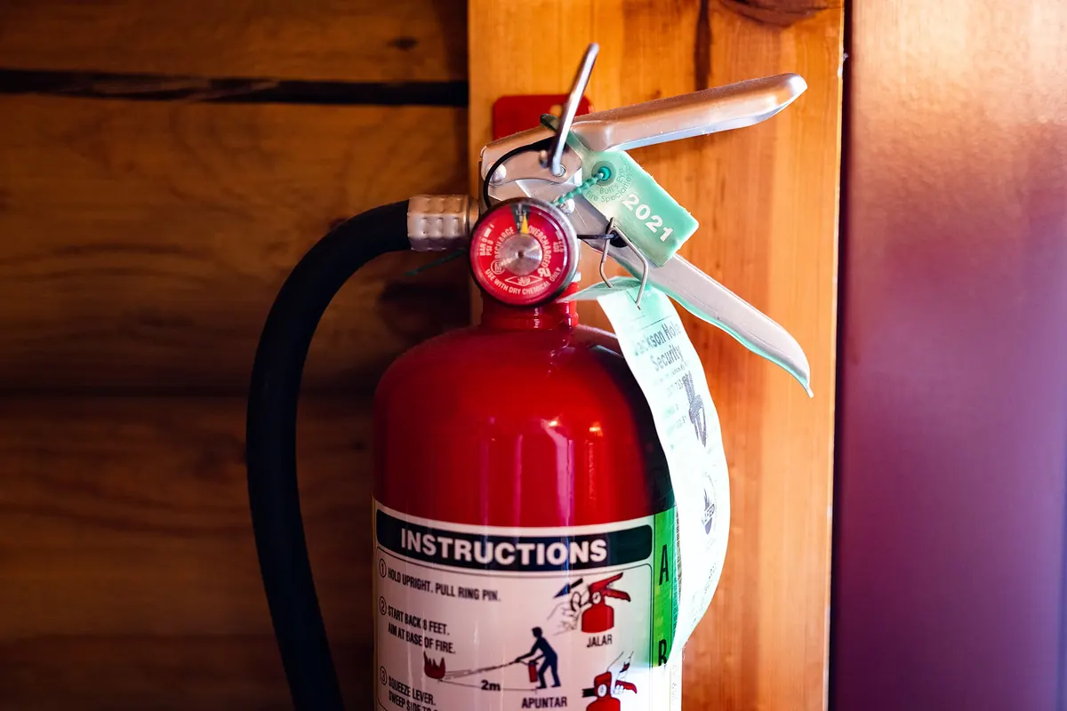 A red portable fire extinguisher with a pin and instructions label hanging on a wooden wall