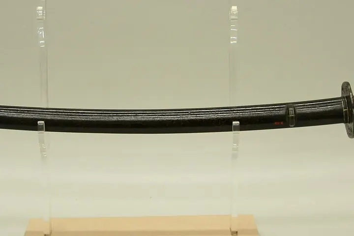A Japanese katana in a dark scabbard displayed horizontally on a wooden stand