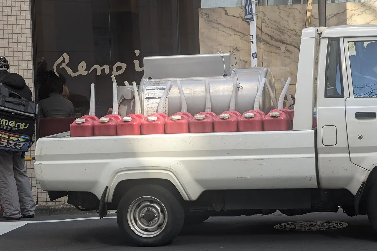 恵比寿の白い軽トラックの荷台に並ぶ赤い燃料缶