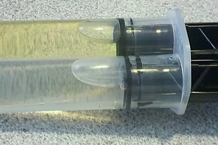 Dual-barrel epoxy adhesive syringe with a black plastic holder on a grey surface