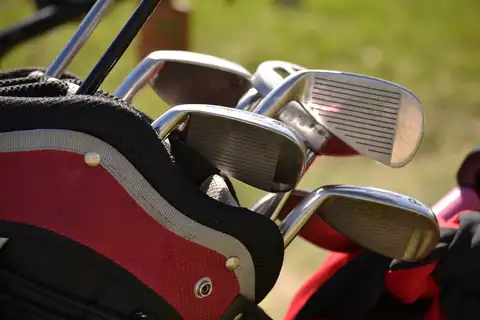Golf club heads sticking out of a red and black golf bag with grass behind