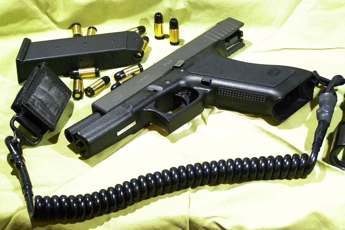 Black replica pistol with a coiled cord, a magazine and brass cartridges on a yellow cloth