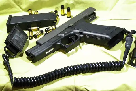 Black replica pistol with a coiled cord, a magazine and brass cartridges on a yellow cloth