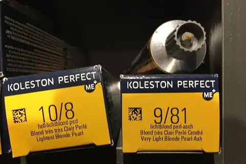 Two yellow and navy boxes of hair dye with a metal tube standing behind them on a dark shelf
