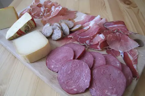 Slices of ham, salami, and sausage with wedges of cheese arranged on a wooden board
