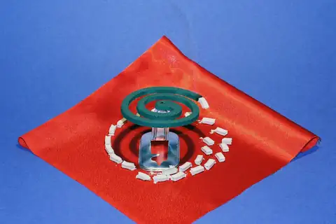 A green coiled mosquito repellent incense on a metal stand with scattered ash on a red cloth over a blue background