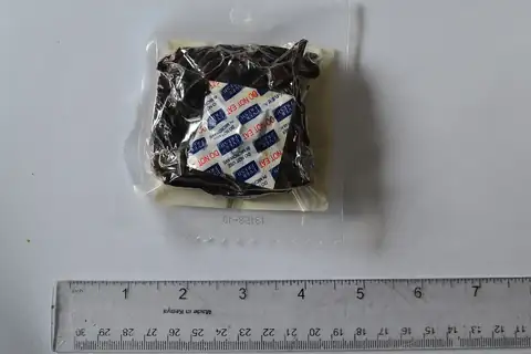 A sealed clear packet of dark beef jerky on a white surface with a ruler below it