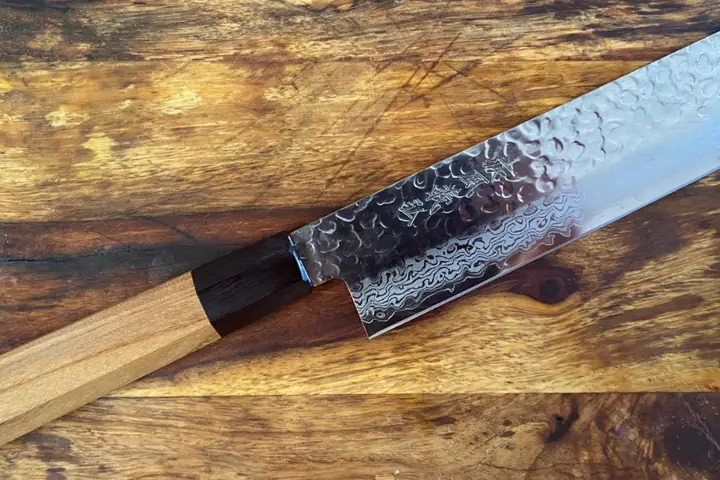 A kitchen knife with a textured blade and a wooden handle lying on a wooden cutting board