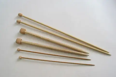Six wooden knitting needles with round knob ends in different shades laid on a white surface