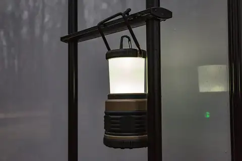 An LED camping lantern hanging from a hook on a metal pole at night