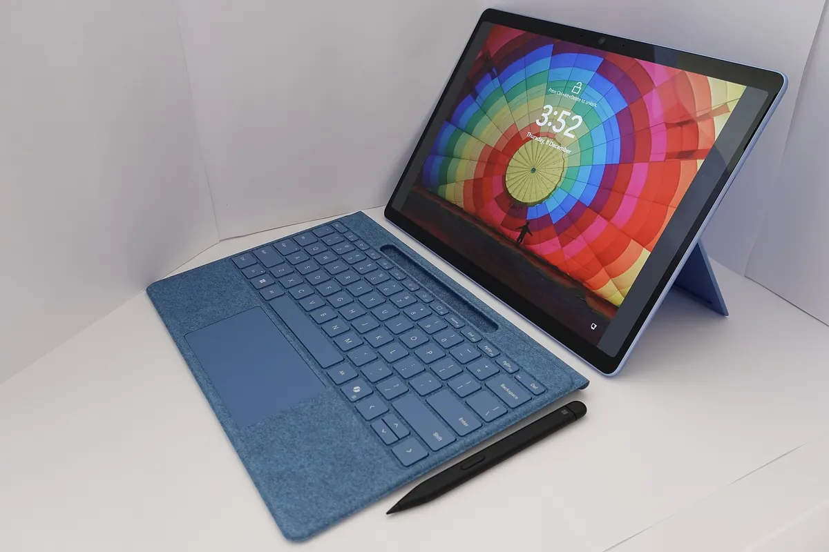 A laptop-style computer with a blue keyboard cover and a stylus pen on a white surface