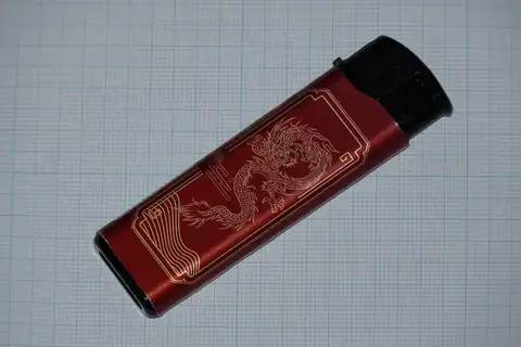 Dark red disposable lighter with a dragon design on a blue grid background