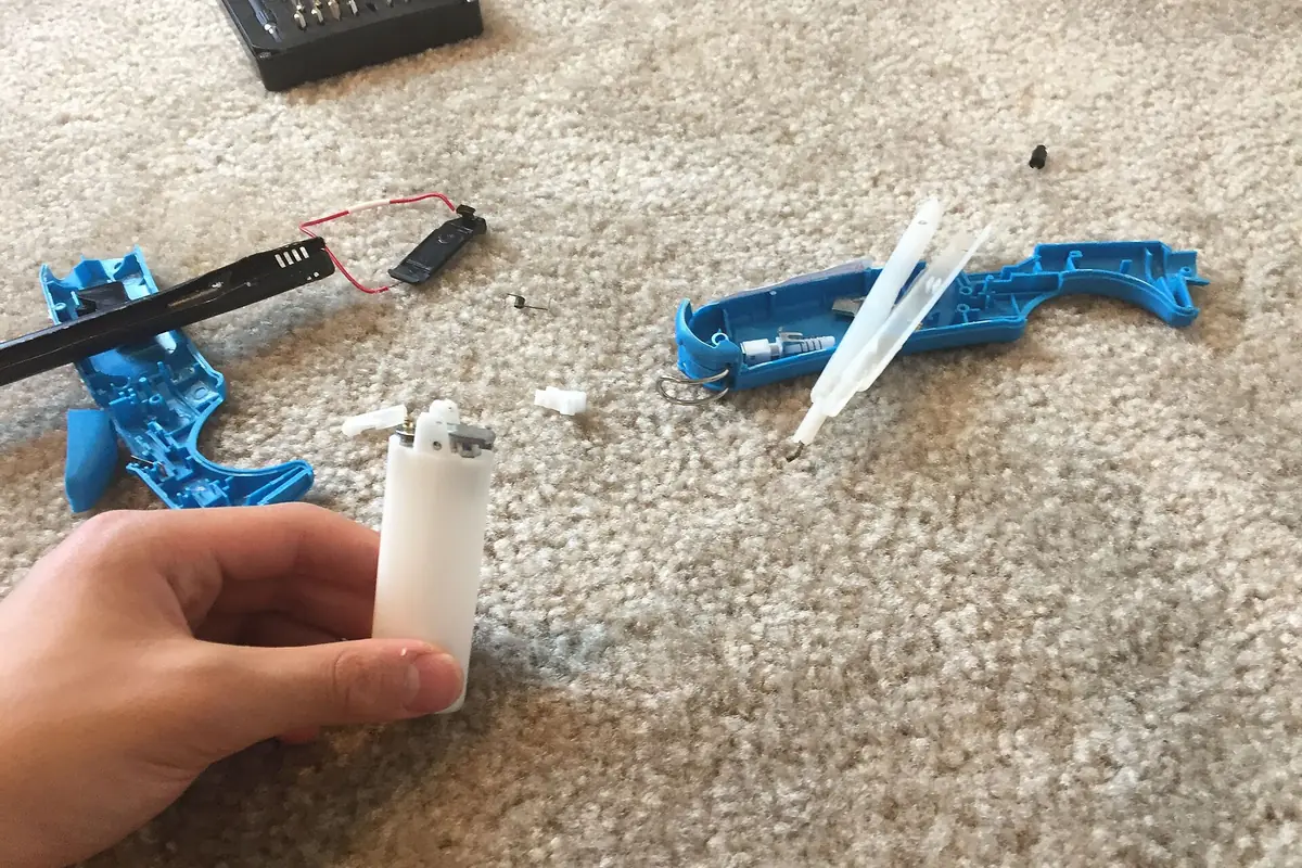 地毯上的一隻手，拿著小型白色打火機燃料罐和藍色打火機零件