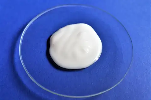 White lotion on a round glass dish against a blue background