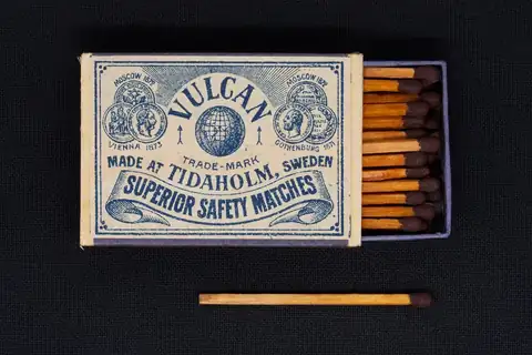 Vulcan Superior Safety Matches box with matches in the open drawer and one match lying in front, on a dark background