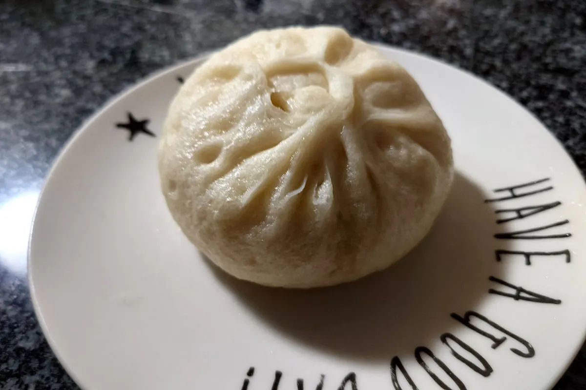 A steamed pork bun (nikuman) on a white plate with a star print and Have a good day text