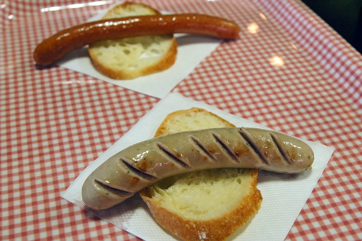 Two grilled sausages on bread over a red-checked tablecloth at the Carl Raymon sausage shop in Hakodate