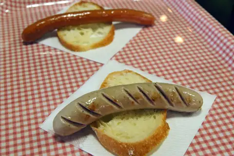 Two grilled sausages on bread over a red-checked tablecloth at the Carl Raymon sausage shop in Hakodate