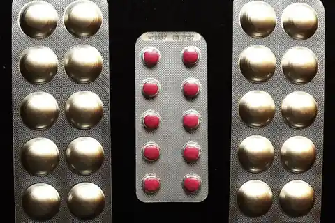 Three blister packs of tablets, two with large silver-sealed pills and one with small red pills, on a black background