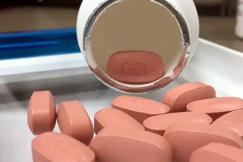Pink oval tablets spilling from a white pill bottle with an open foil seal onto a tray