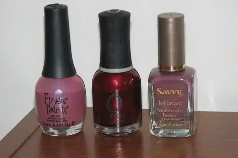 Three bottles of nail polish in pink, dark red and mauve colors on a wooden table