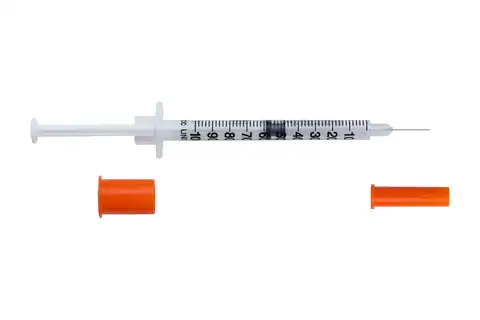 An insulin syringe with its needle exposed and two orange caps removed beside it on a white background