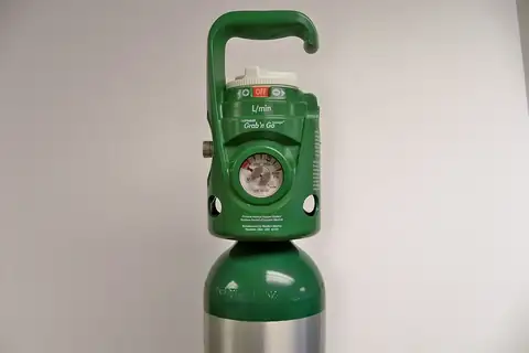 A green portable oxygen cylinder with a carrying handle, a pressure gauge, and an OFF dial on top