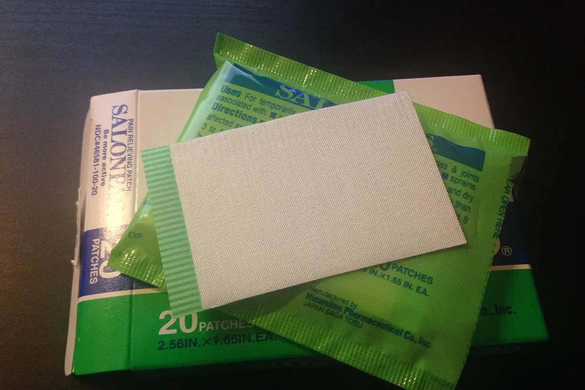 A Salonpas pain relief patch box with a green foil packet and one white patch on top