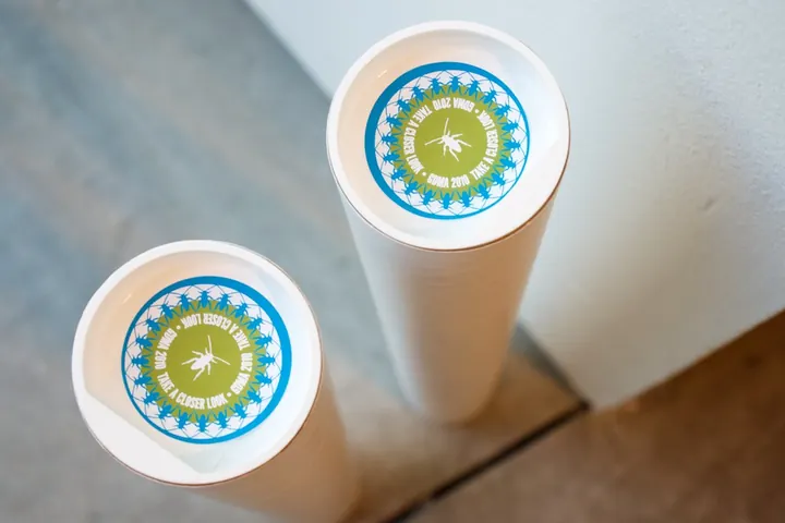 Two white poster tubes standing on a floor, each with a round blue and green label on its end
