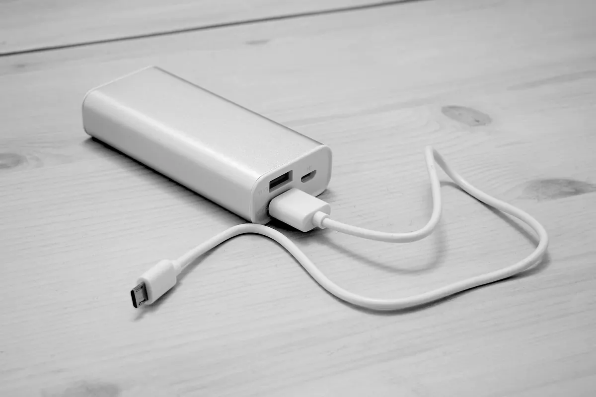 A silver portable power bank with a white cable plugged into it, on a wooden surface