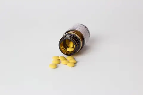An amber pill bottle lying on its side with yellow pills spilled onto a white surface