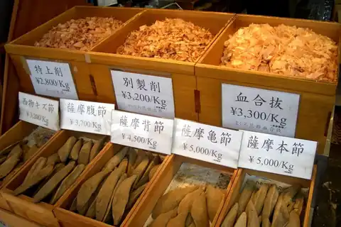 Wooden boxes of dried bonito flakes (katsuobushi) and whole blocks with Japanese price labels at a market stall