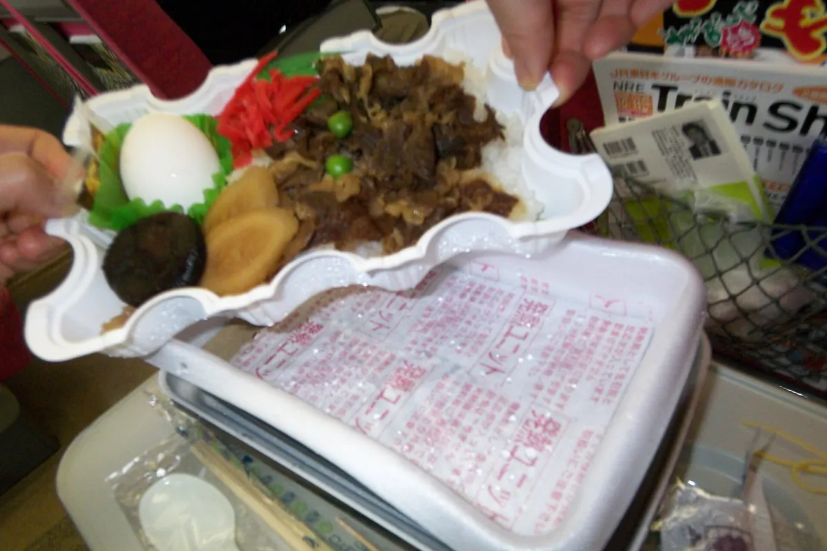 Open Japanese beef bento with a boiled egg and pickles above a white self-heating tray