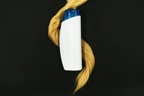 A white shampoo bottle with a blue cap and a blonde hair weft twisted around it on a black background