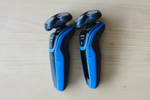 Two blue Philips rotary electric shavers standing side by side on a wooden table