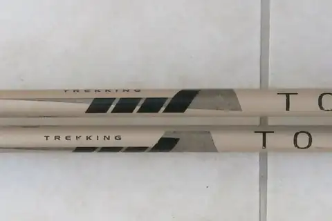 A pair of retracted trekking poles lying side by side on a light tiled floor