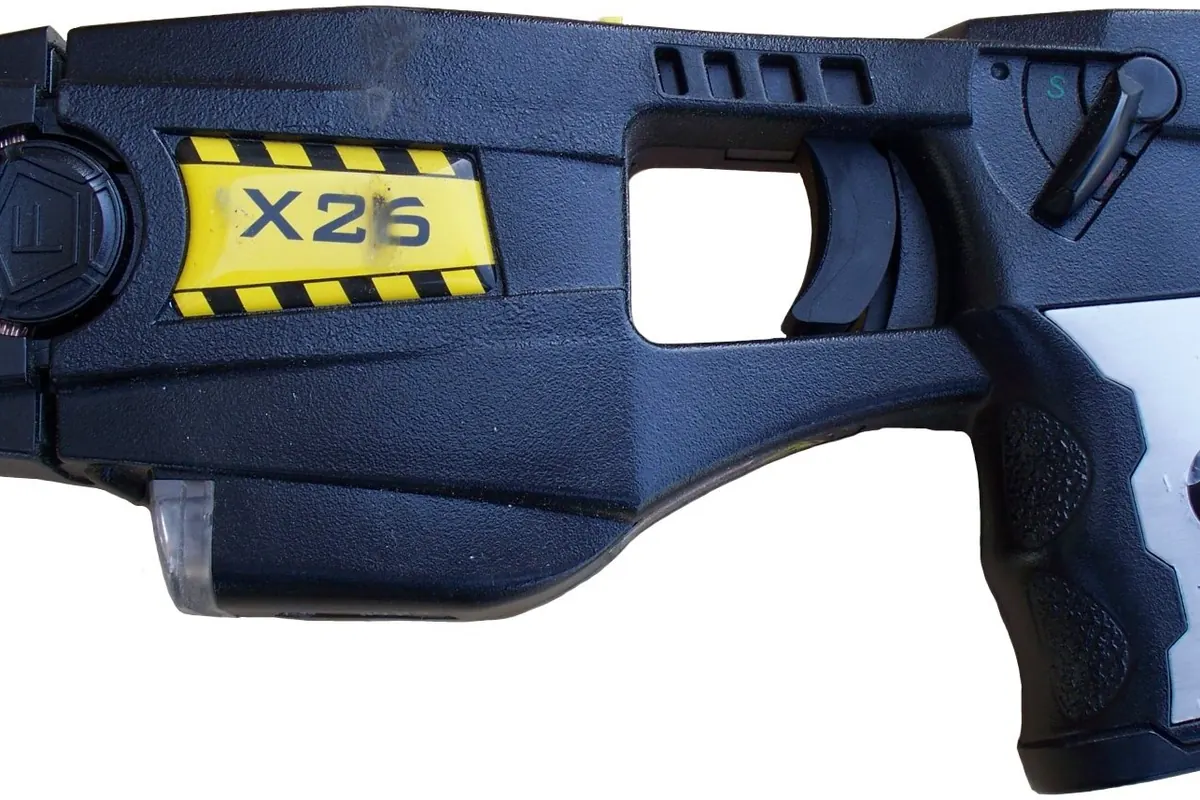 A black X26 TASER stun gun with yellow and black warning stripes on a white background