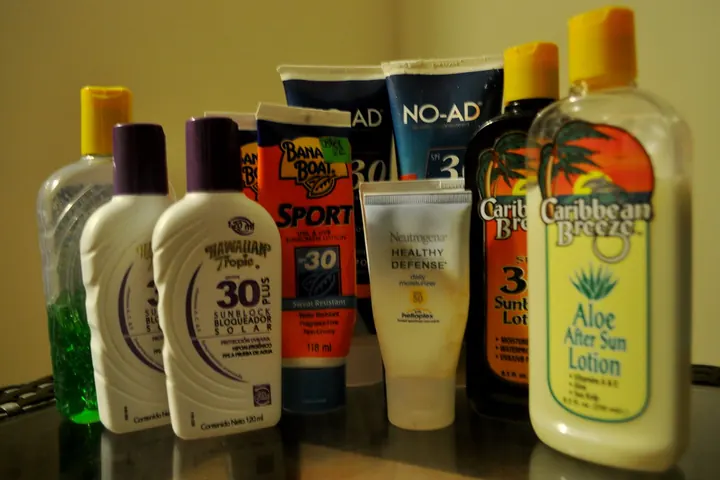 Bottles and tubes of sunscreen and after-sun lotion in different sizes lined up on a dark surface