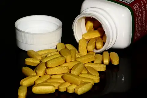Yellow supplement tablets spilling out of a white bottle onto a black surface