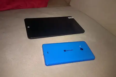 A black tablet and a blue smartphone lying side by side on a beige surface