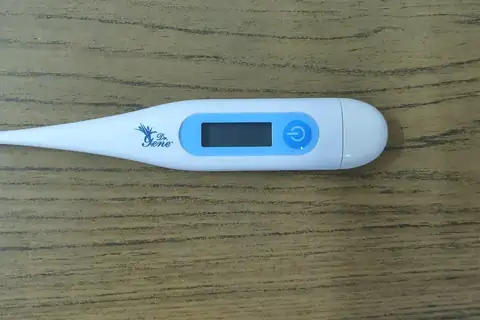 A white digital thermometer with a light blue display panel lying on a wooden table