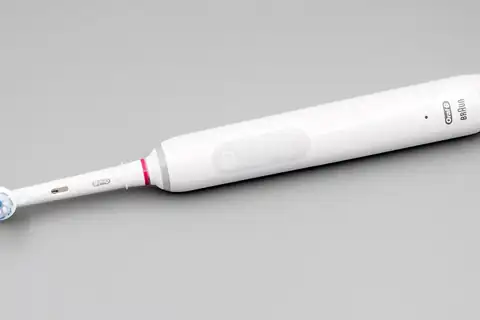 A white Oral-B electric toothbrush lying diagonally on a grey background