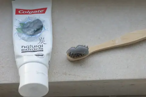 A Colgate charcoal toothpaste tube beside a bamboo toothbrush on a beige counter