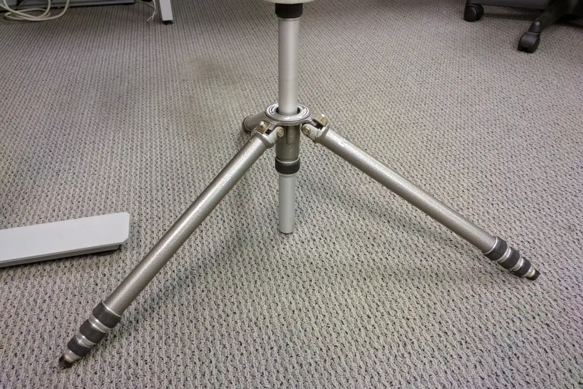 A camera tripod with its legs spread wide, standing on a carpet