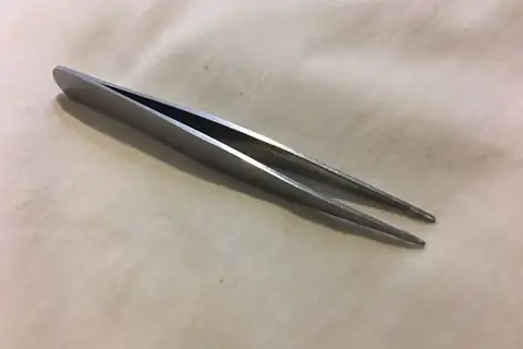 Pair of metal tweezers with narrow pointed tips lying diagonally on a light beige cloth