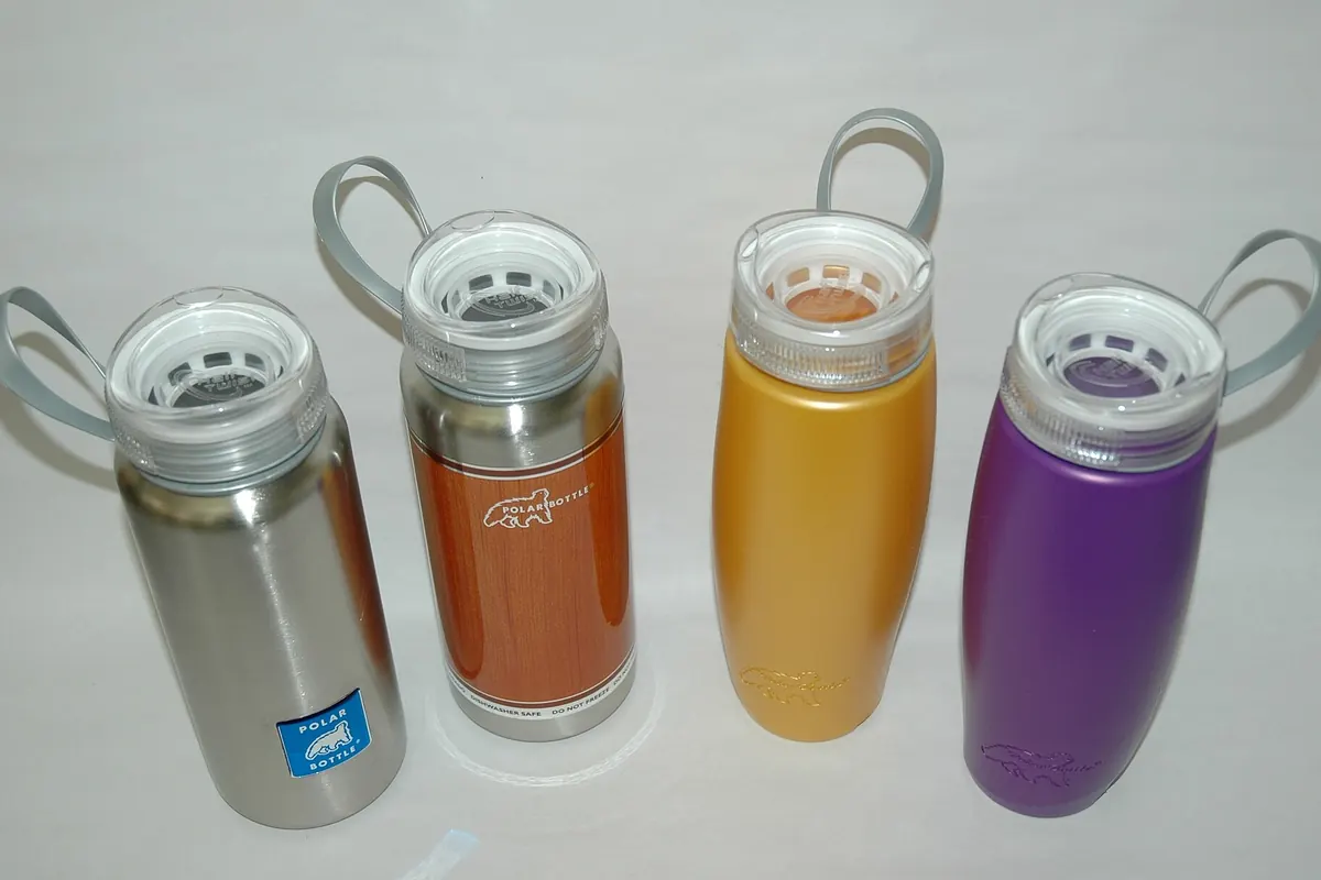 Four Polar Bottle metal water bottles in different colors with loop-handle lids, lined up on a white background