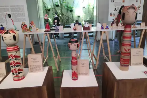 Wooden kokeshi dolls with painted faces and red patterns displayed on white stands