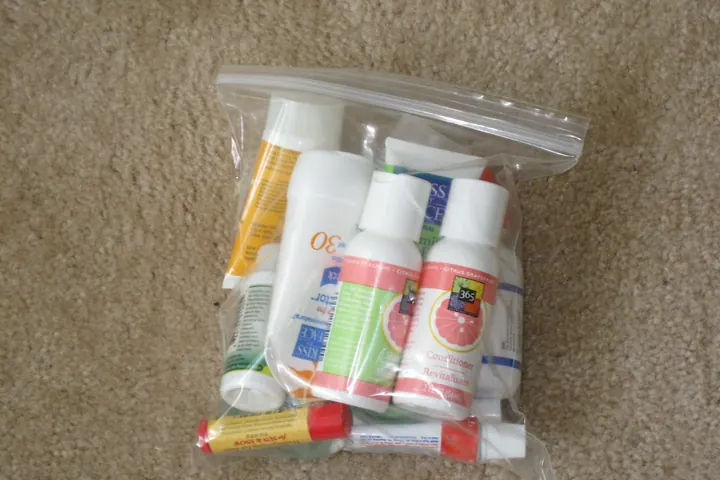 A clear zip-top plastic bag holding small toiletry bottles and tubes on a beige carpet