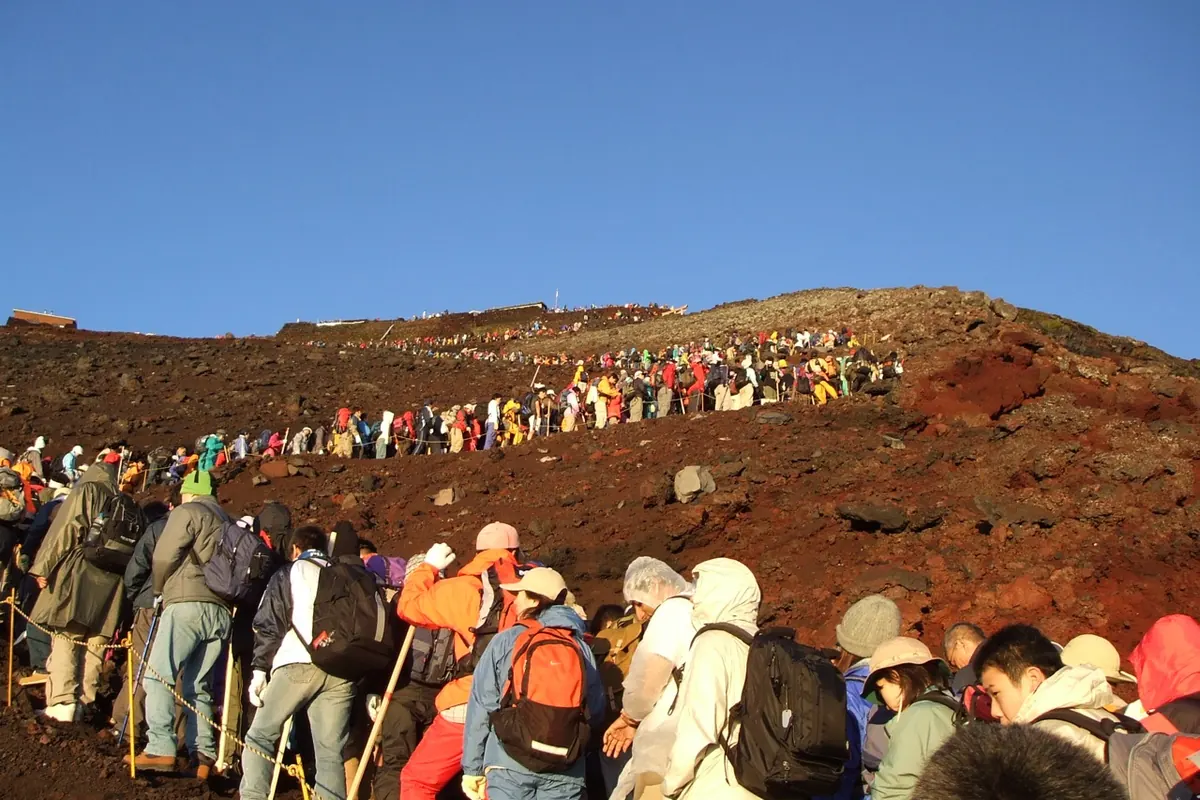 富士山偏红色的岩石斜坡上,穿着彩色外套、排成长队的登山者