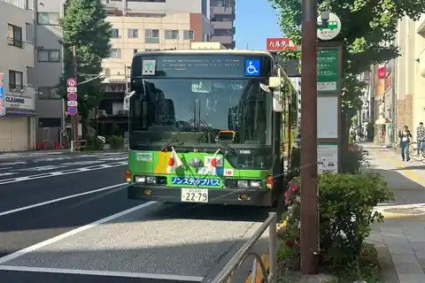 A green Tokyo city bus with two small Japanese flags on its front, stopped at a bus stop in Asakusa, Tokyo